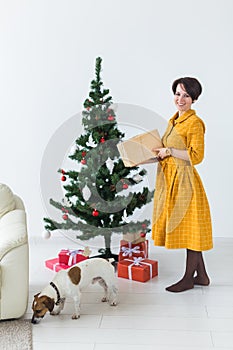 Happy young woman with lovely dog opening present box under christmas tree. Holidays concept