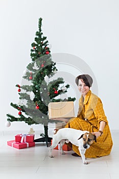 Happy young woman with lovely dog opening present box under christmas tree. Holidays concept.