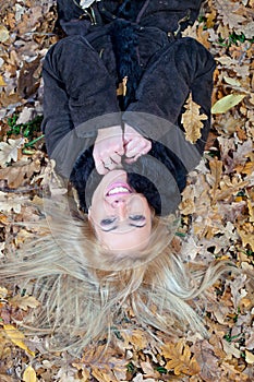 Happy young woman lying down in autumn leaves