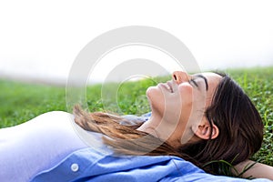 Happy young woman lying down on grass relaxing in a park in the city.