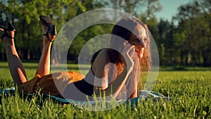 Happy Young Woman Lying on Green Lawn and Talking on the Phone or Smartphone.