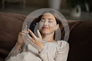 Happy young woman lying on sofa browse web on smartphone