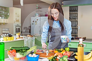 Happy young woman making cake smearing a layer with cream standing in kitchen