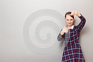 Happy young woman is making frame with fingers near face and smiling