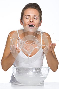 Happy young woman making water splashes while washing face