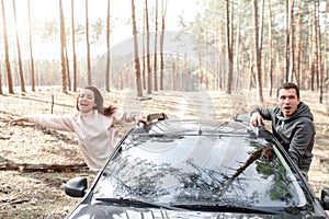 Happy young woman and man climbed out of a car window. Traveling by car in the forest. Country trip. Vacation by car