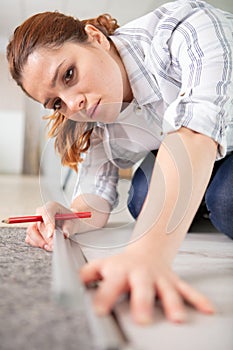 happy young woman measuring and marking laminate floor tile