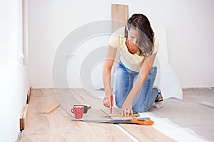 Happy young woman measuring and marking laminate floor tile for cutting