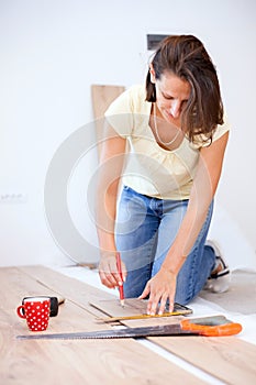 Happy young woman measuring and marking laminate floor tile installing laminate flooring in new apartment