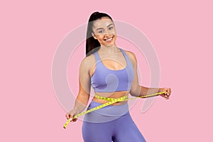 Happy young woman with measuring tape around waist