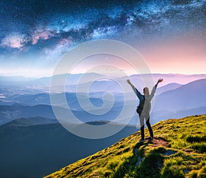 Happy young woman on the mountain peak and arched Milky Way