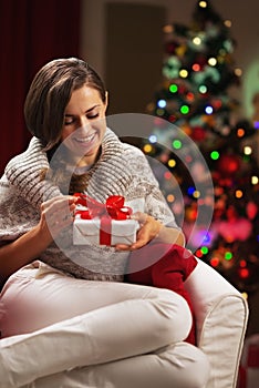 Happy young woman near christmas tree holding present box