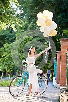 Happy young woman near vintage bicycle holding air balloons