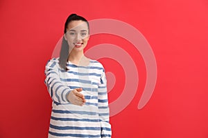 Happy young woman offering handshake against red background, focus on hand. Space for text