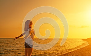 Happy young woman open her arms to the sky and sea at sunset