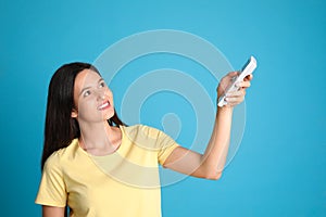 Happy young woman operating air conditioner with remote control on light blue