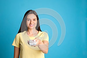 Happy young woman operating air conditioner with remote control on light blue background. Space for