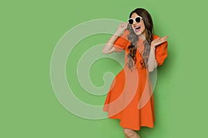 Happy young woman in orange mini dress and sunglasses is shouting