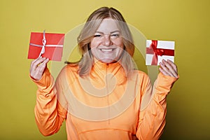 Happy young woman in orange t-shirt holds two gift certificates isolated on yellow background. People lifestyle holidays concept