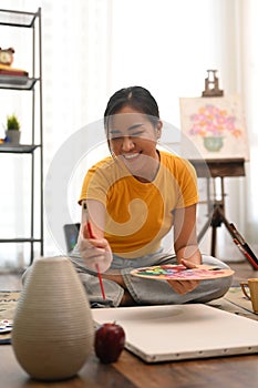 Happy young woman painting picture with watercolor at cozy home. Art, creative hobby and leisure activity concept