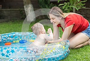 Happy young woman palying with her baby boy swimming in inflatable pool