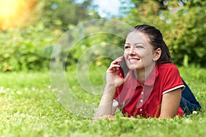 Happy young woman in the park smiling and talking on smartphone. beautiful girl get a good news on her mobile phone. leisure in na