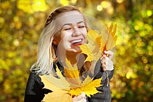 Happy young woman in park on sunny autumn day. Cheerful beautiful girl in gray sweater outdoors on beautiful fall day.