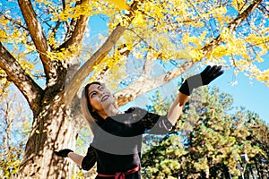 Happy young woman in park on sunny autumn day, laughing, playing leaves. Cheerful beautiful girl in black retro dress autumn fashi