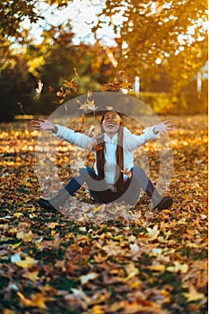 Happy young woman in park on sunny autumn day, laughing, playing leaves. Cheerful beautiful girl in white sweater during autumn se