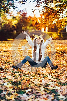 Happy young woman in park on sunny autumn day, laughing, playing leaves. Cheerful beautiful girl in white sweater during autumn se