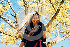 Happy young woman in park on sunny autumn day, smiling. Cheerful beautiful girl in black retro dress autumn fashion style