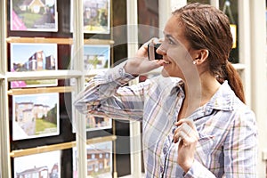 Happy Young Woman On Phone Outside Estate Agents