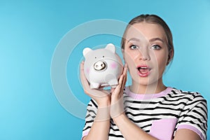 Happy young woman with piggy bank and space for text on color background