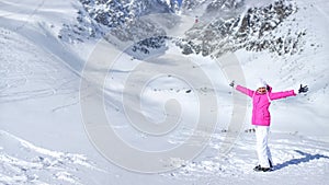Happy young woman in pink ski jacket, gloves, hat and ski boots