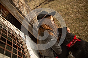 Happy young woman plaing with her black dog Brovko Vivchar in fron of old wooden house