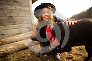 Happy young woman plaing with her black dog Brovko Vivchar in fron of old wooden house