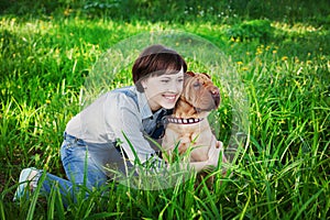 Happy young woman playing with dog Shar Pei in the green grass, true friends forever