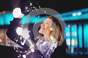 Happy young woman playing with fairy lights at winter evening in