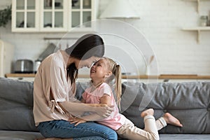 Happy young woman playing with laughing little daughter on sofa.