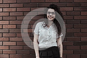 Happy young woman posing on camera on the red brick wall background