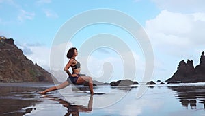 Happy young woman practicing yoga on the beach at sunset. Healthy active lifestyle concept. Slow motion