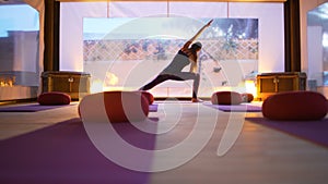 Happy young woman practicing yoga on the empty class at sunset.