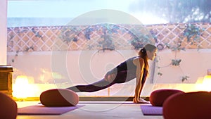 Happy young woman practicing yoga on the empty class at sunset.