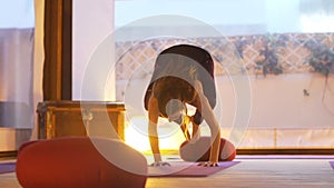 Happy young woman practicing yoga on the empty class at sunset.