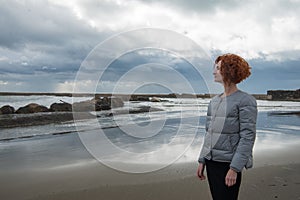 happy young woman in puffer jacket on seashore on cloudy day photo