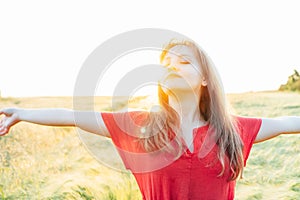 A happy young woman with raised arms relaxing in wheat field on sunset. Breathe of freedom. Positive emotions feeling