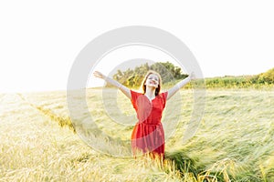 A happy young woman with raised arms relaxing in wheat field on sunset. Celebrating freedom. Positive emotions feeling