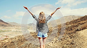 Happy young woman raises hands up on a hiking trail on top of the mountain, view from the back, Tenerife, Canary Islands