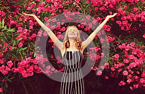 Happy young woman raises hands up over pink roses flowers