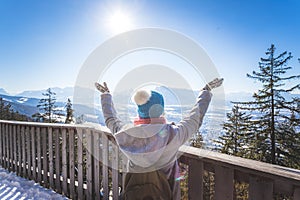 Happy young woman is raising her hands on the mountain, enjoying the view over Salzburg. Winter time on Gaisberg, Salzburg,